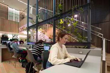 group of students sitting in an open space working on their laptops at a counter