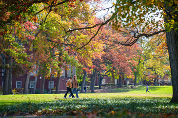 Two students walking across a lush green field surrounded by fall foliage on Vanderbilt University campus
