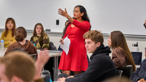 A woman in a red dress is giving a lecture to a group of students.