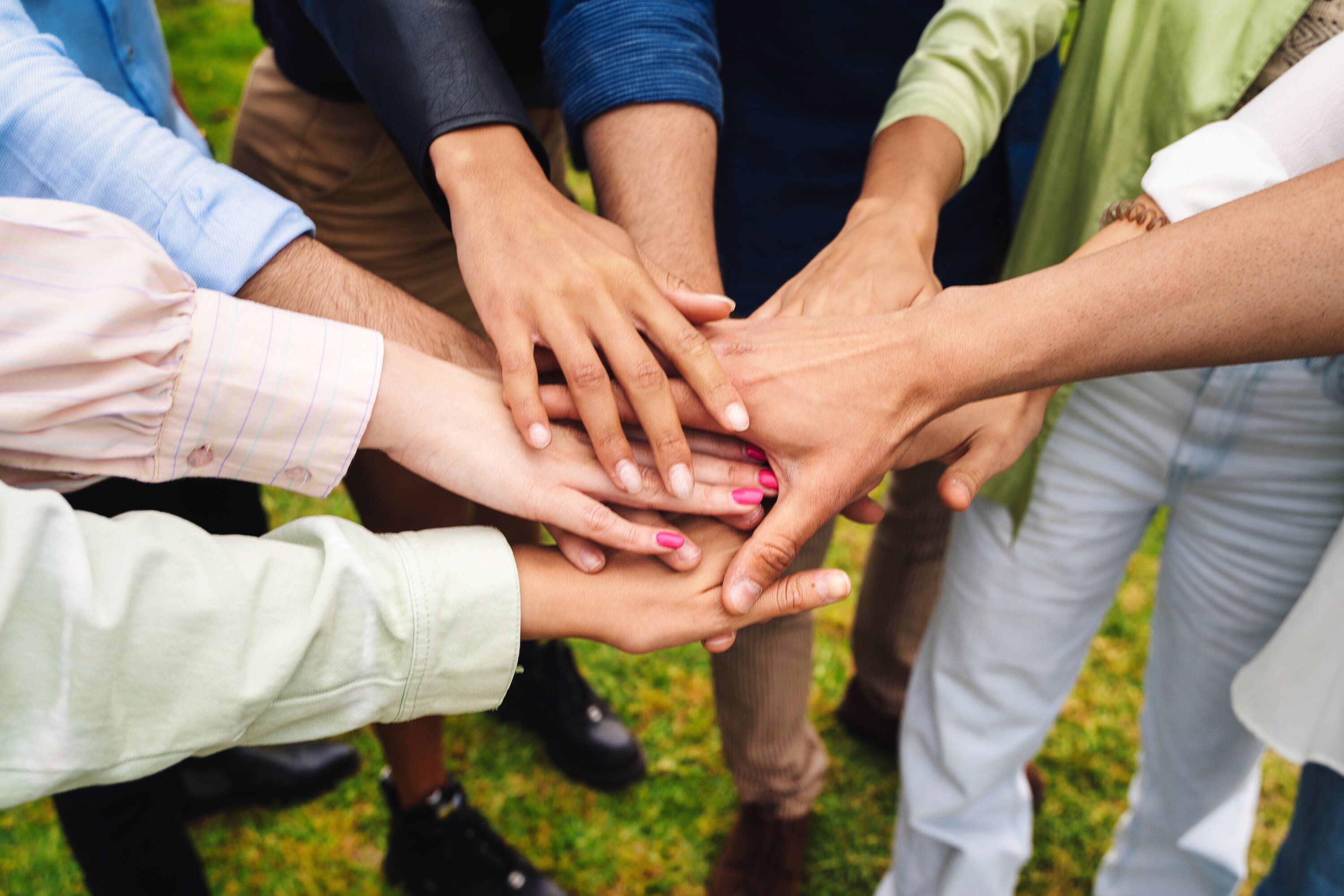 Diverse group stacking hands outdoors showing unity teamwork and collaboration